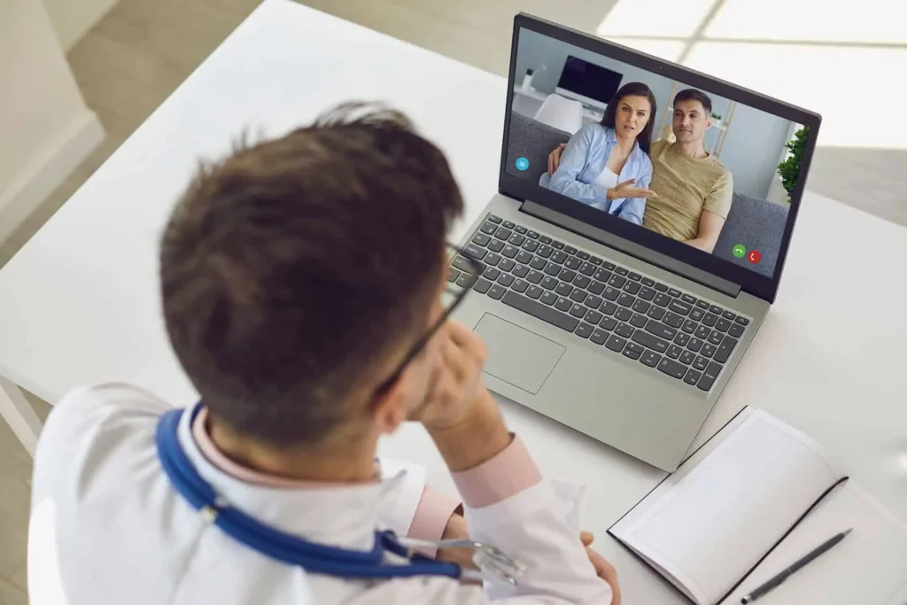 Doctor wearing a stethoscope having a video call with a couple on a laptop.