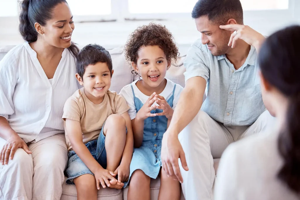 Smiling family sitting together on a couch, father adjusting his daughter's curly hair while mother and son look on.