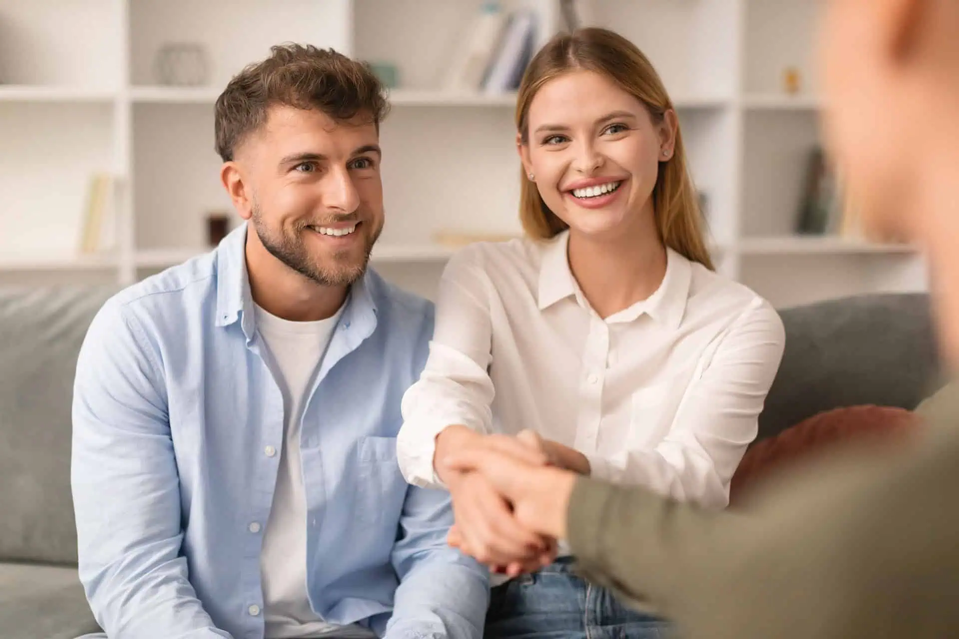 Smiling couple sitting on a couch shaking hands with another person, possibly a counsellor.
