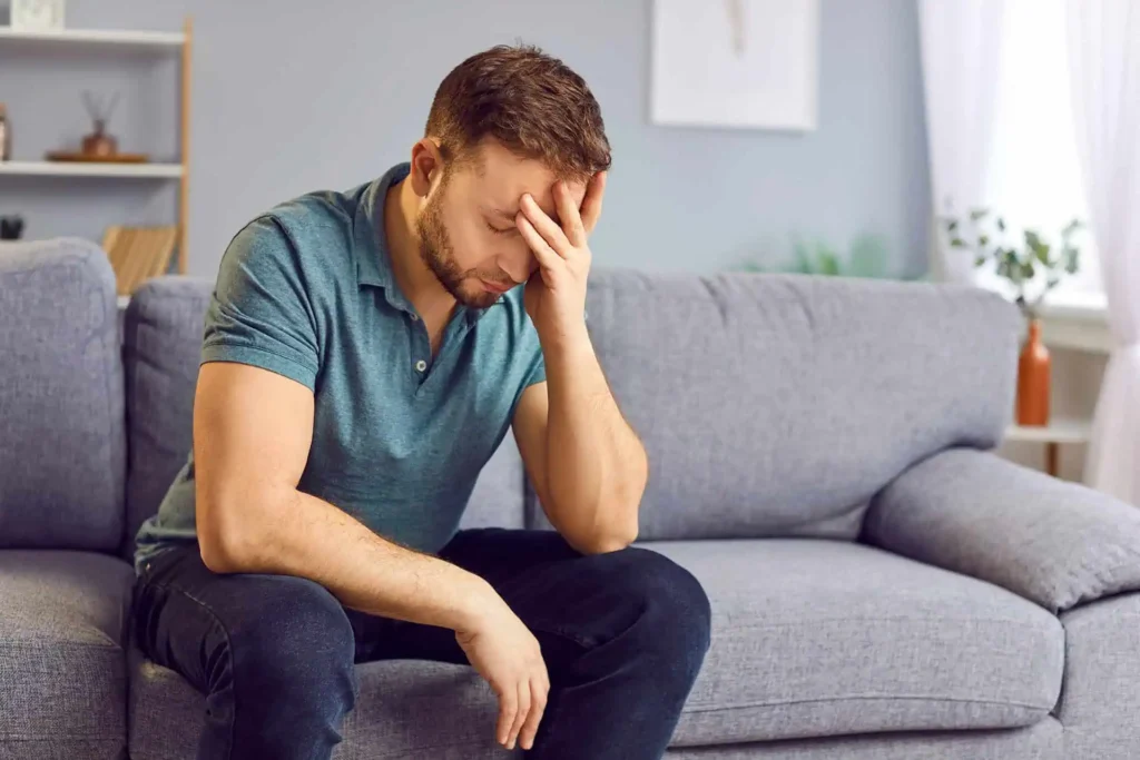 Young man sitting on a couch with his head in his hand, looking stressed or upset.