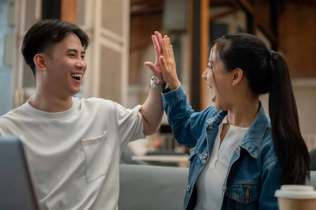 Young man and woman giving each other a high five and laughing in a casual indoor setting.