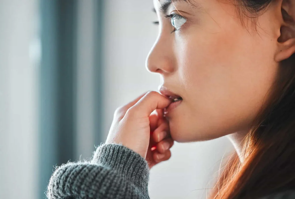 Close-up profile of a worried young woman biting her nails, with a pensive expression.
