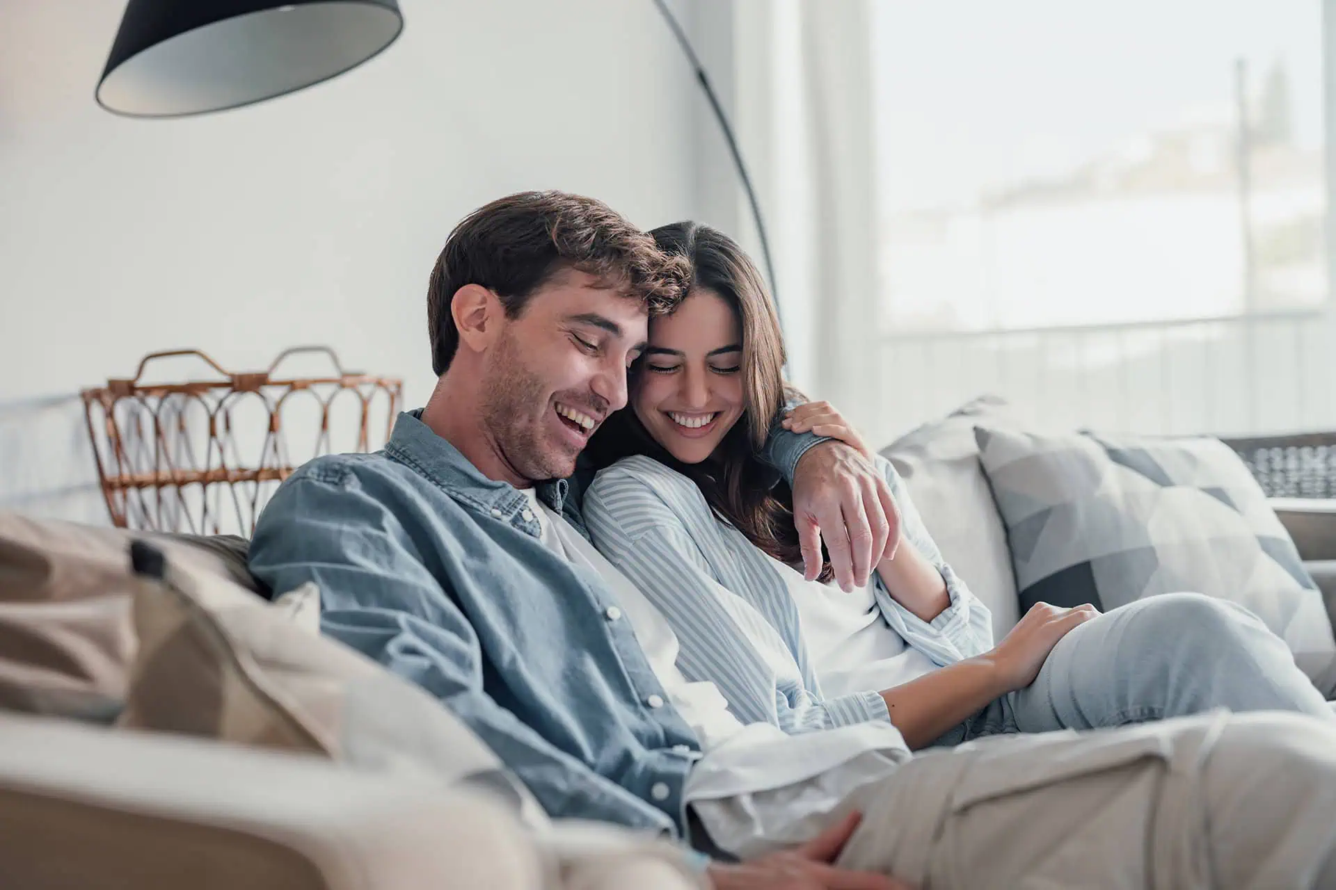 Happy couple snuggling on a couch, smiling together while looking at something in the man's hands.
