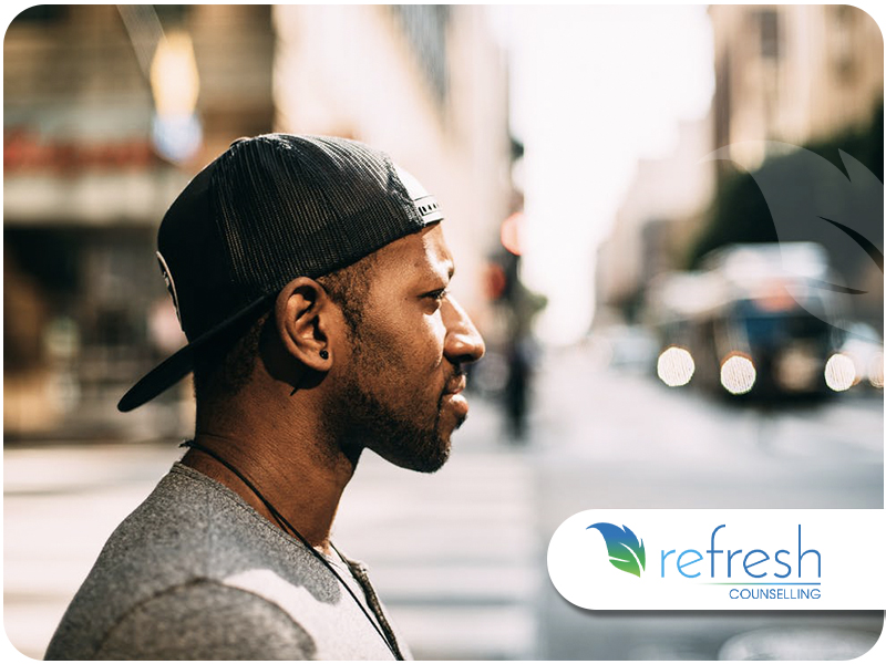 Profile of a young African-American man wearing a baseball cap, looking away on a city street.