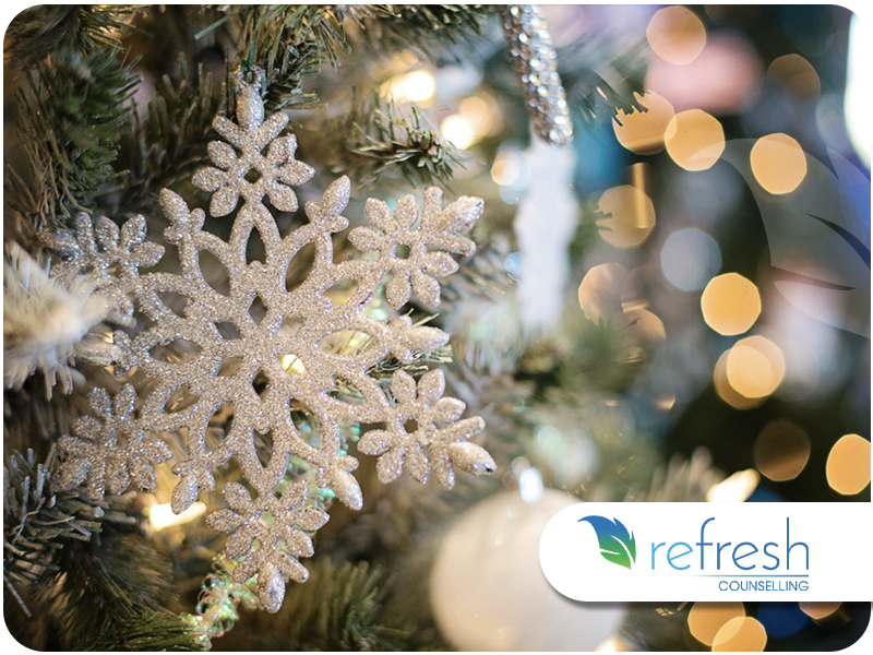 Close-up of a glittery snowflake ornament hanging on a Christmas tree with blurred golden lights.