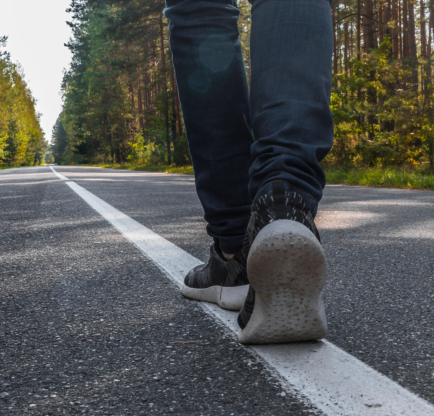 Close-up of a person walking on a paved road wearing sneakers, viewed from behind.