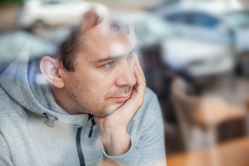 Man in a gray hoodie resting his head on his hand, looking contemplative.