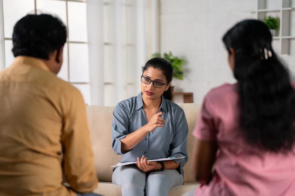 Female therapist with notepad listening attentively to a couple during a counseling session.