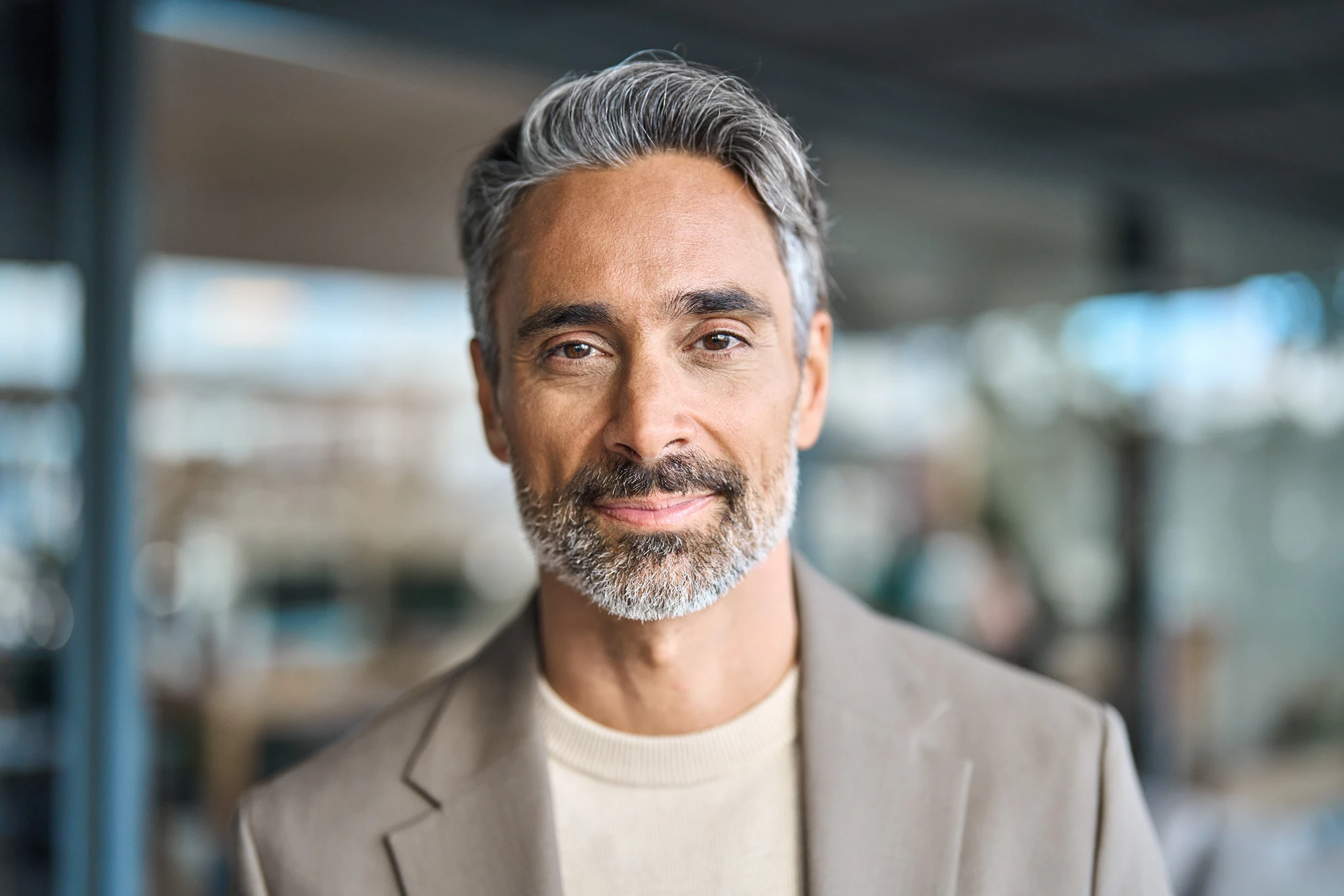 Portrait of a mature man with gray hair and beard smiling softly, wearing a beige jacket.