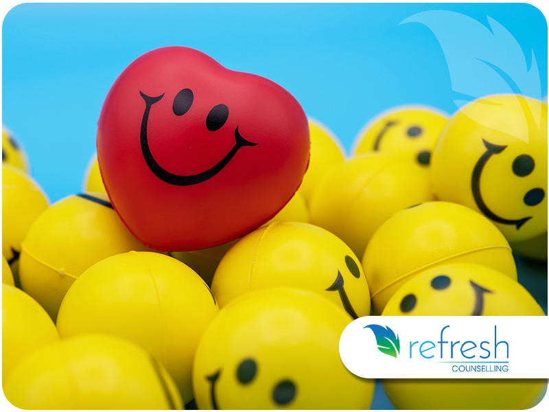 Red heart-shaped stress ball with a smiley face resting on top of yellow smiley stress balls.