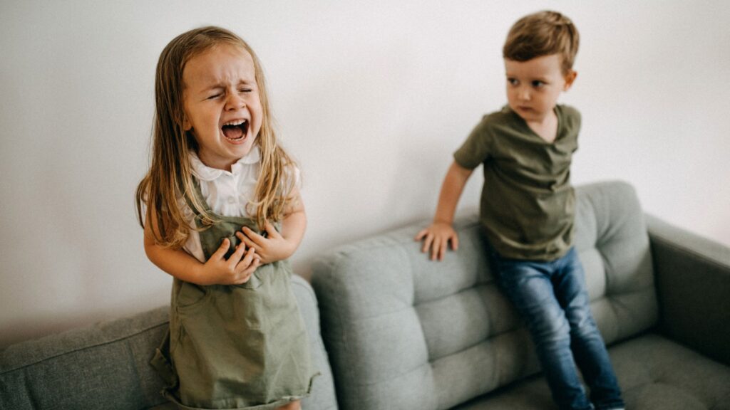 Young girl having an emotional outburst while her brother watches, demonstrating common child mood swings at home