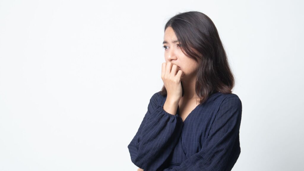 A person in a dark blue shirt biting their nails, displaying anxiety, with a plain white background.