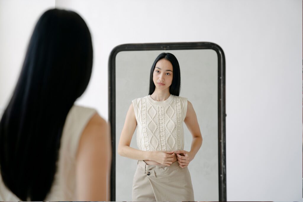 Woman looking at her reflection, representing body image and self-esteem concerns.